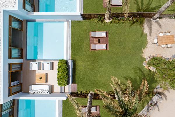 Luftaufnahme des Amirandes Grecotel Boutique Resorts mit Swimmingpool, Liegestühlen und Esstisch im Freien.