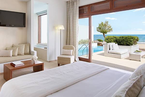 Innenansicht eines Zimmers im Amirandes Grecotel Boutique Resort mit Blick auf den Pool und das Meer.