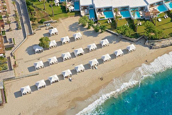 Luftaufnahme des Amirandes Grecotel Boutique Resorts mit vielen weißen Strandpavillons und einem blauen Meer.