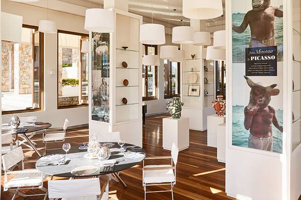 Innenraum des Amirandes Grecotel Boutique Resort mit Esstischen, Stühlen und einer großen Anzeigetafel mit einem Bild von Picasso.