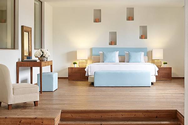 Schlafzimmer im Amirandes Grecotel Boutique Resort mit einem großen Bett, blauen Kissen, zwei Nachttischen, einem Stuhl und einem Tisch mit einer Blumenvase.