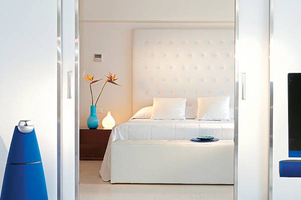 Schlafzimmer im Amirandes Grecotel Boutique Resort mit weißem Bett, Kissen und Fernseher.