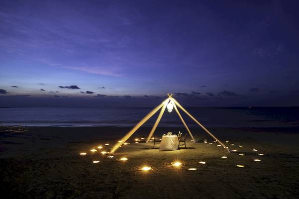 Romantisches Essen auf dem Strand bei Nacht mit einem Tisch und einem Zelt, das von Kerzen umgeben ist.