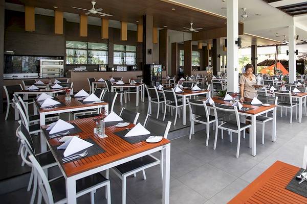 Innenrestaurant des Kantary Beach Hotel, Villas & Suites mit gedeckten Tischen und einer wartenden Angestellten.