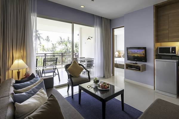Wohnzimmer im Kantary Beach Hotel mit Fernseher, Kühlschrank und Balkonzugang.