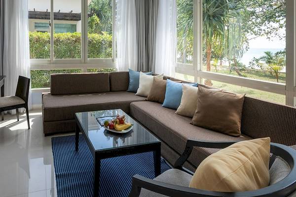 Wohnbereich des Kantary Beach Hotel mit Sofa, Tisch, Fernseher und Aussicht auf den Ozean.