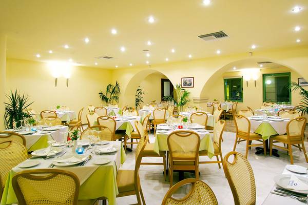 Innenansicht des Restaurants im Giannoulis Grand Bay Beach Resort mit gedeckten Tischen und Stühlen.