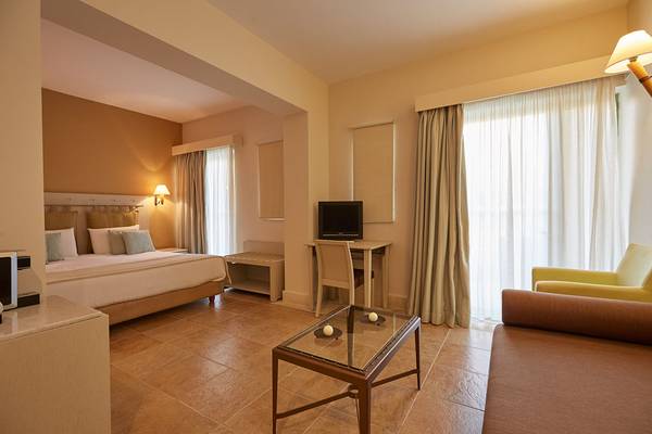 Ein modernes Zimmer im Giannoulis Grand Bay Beach Resort mit einem Bett, Schreibtisch und einem Wohnzimmerbereich.