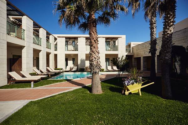 Außenbereich des Giannoulis Grand Bay Beach Resorts mit Swimmingpool, Liegestühlen und Palmen.