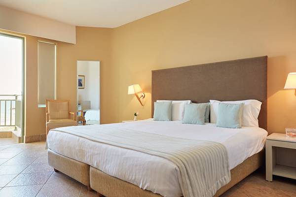 Hotelzimmer im Giannoulis Grand Bay Beach Resort mit großem Bett, Sesseln und Fenstern.