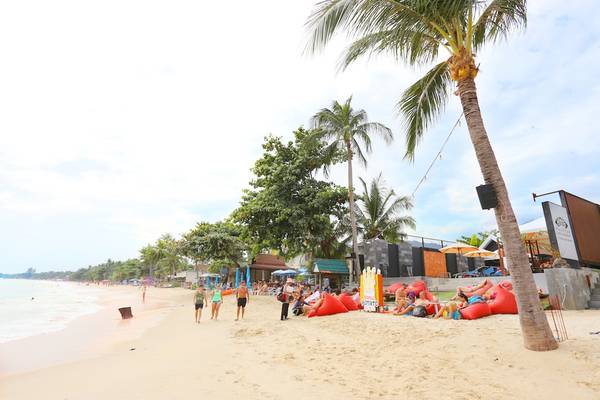 Strandszenerie des Pavilion Samui Villas & Resort mit Palmen, roten Sesseln und Besuchern.