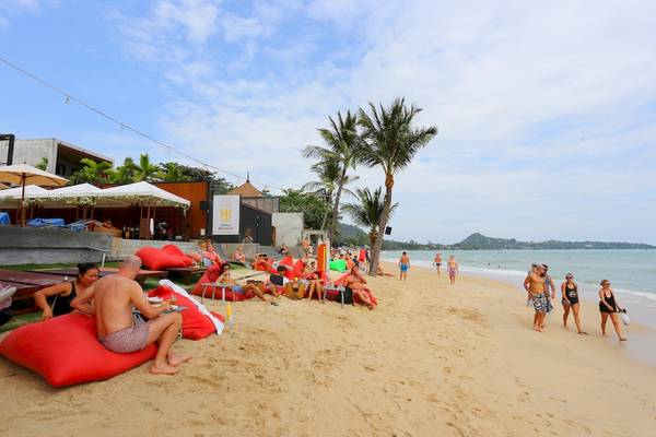 Besucher entspannen auf roten Liegestühlen am Strand des Pavilion Samui Villas & Resort.
