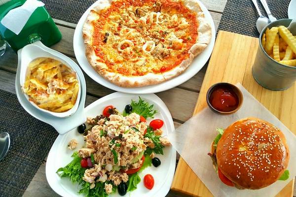 Verschiedene Teller mit Essen auf einem Holztisch, einschließlich einer Pizza, einem Salat, einem Burger und frittierten Pommes.