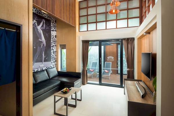 Innenansicht eines Zimmers im Pavilion Samui Villas & Resort mit einem schwarzen Sofa, einem Tisch, einem Fernseher und einer Schiebetür.