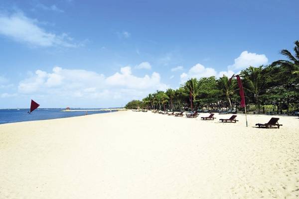 Strand des Mercure Resort Sanur mit weißen Sand, braunen Sonnenliegen und Palmen