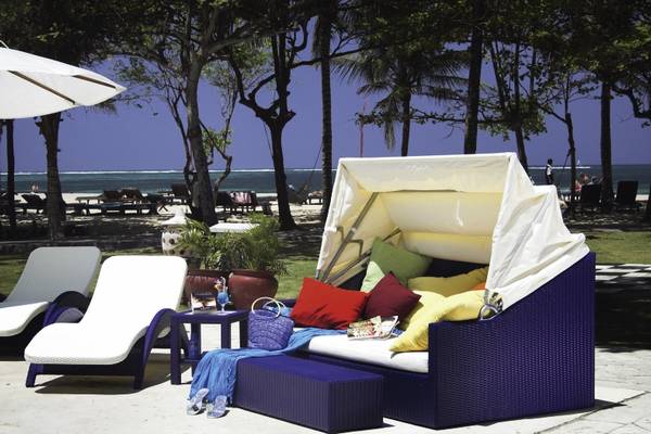 Loungebereich am Strand des Mercure Resort Sanur mit einem blauen Sonnenbett und weißen Liegestühlen.
