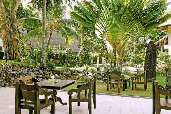 Außenbereich des Mercure Resort Sanur mit Tischen und Stühlen in einem Garten.