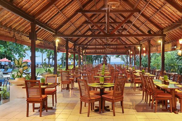 Außenbereich des Mercure Resort Sanur Restaurants mit braunen Holztischen und Stühlen.