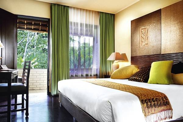 Schlafzimmer im Mercure Resort Sanur mit großem Bett, grünen Vorhängen und Blick auf Bäume.
