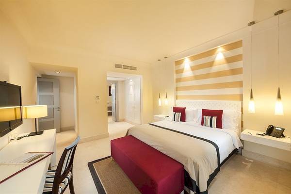 Juweira Boutique Hotel Zimmer mit großem Bett, Fernseher, Schreibtisch und roten Akzenten.