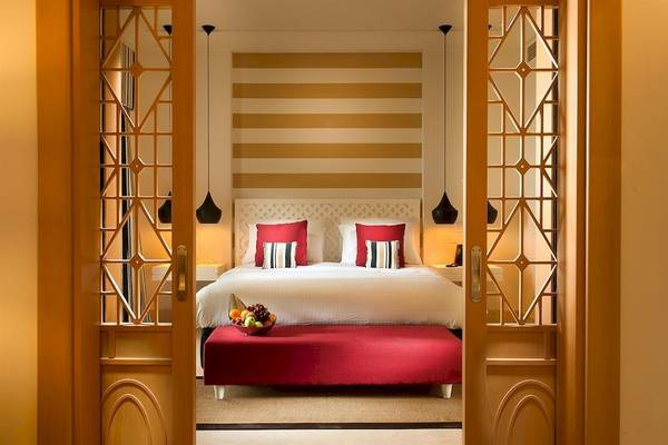 Schlafzimmer im Juweira Boutique Hotel mit rotem Ottomane und Früchteschalen auf dem Bett.