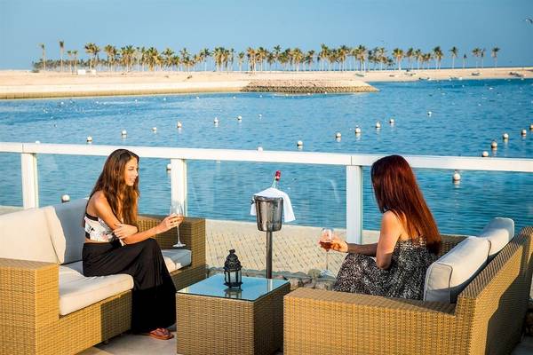 Zwei Frauen auf einer Terrasse mit Blick auf das Meer und Palmen