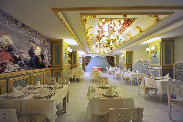 Innenansicht des Restaurants im Seaden Corolla Hotel mit kunstvollen Deckengemälden, Tischdekorationen und geometrischen Wandmustern.