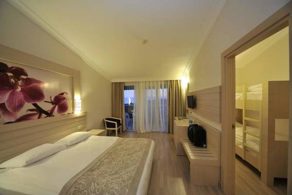 Innenansicht eines Zimmers im Seaden Corolla Hotel mit Doppelbett, Nachttisch, Fernseher und Balkon.