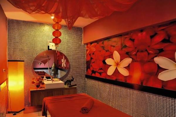 Spa-Behandlungsraum im Seaden Corolla Hotel mit rotem Dekor, großen Blumentapeten und Entspannungsmöbeln.