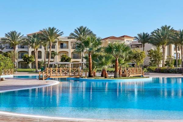 Außenpool des Jaz Mirabel Beach Hotels mit Gebäuden und Palmen im Hintergrund.