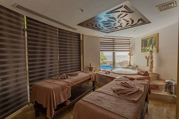 Spa-Behandlungsraum im Sunrise Queen Luxury Hotel mit zwei Massagetischen, Blick auf einen Pool und Meer.