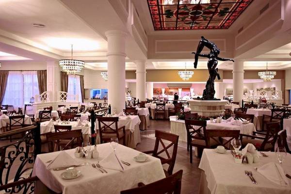 Esszimmer im Bahia Principe Luxury Esmeralda Hotel mit Tisch, Stühlen, Statue und Kronleuchtern.