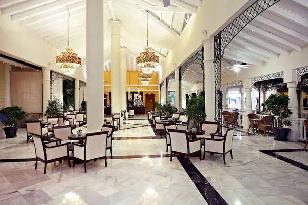 Foyer des Bahia Principe Luxury Esmeralda Hotels mit weißen Tischen und Sesseln, Kronleuchtern und Pflanzen.