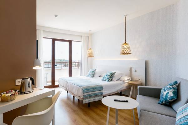 Doppelbettzimmer im Leonardo Royal Hotel Ibiza Santa Eulalia mit Balkon, Schreibtisch und Sofa.