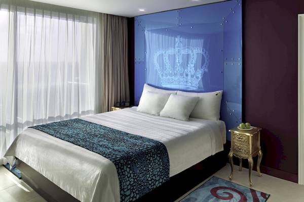 Innenansicht eines Zimmers im Hard Rock Hotel Cancun mit einem Bett, Tisch und einer Tür zum Essbereich.