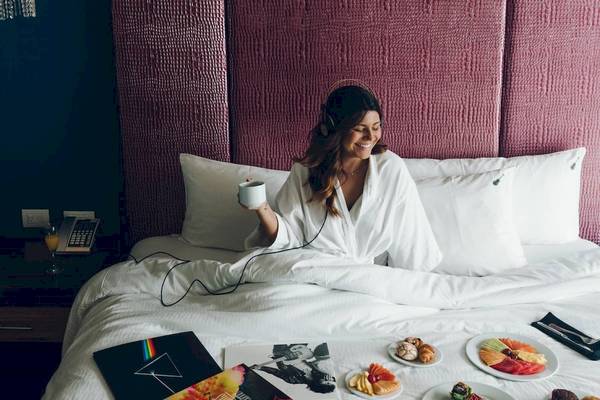 Frau im weißen Bademantel im Bett mit Frühstück und Kopfhörern im Hard Rock Hotel Cancun