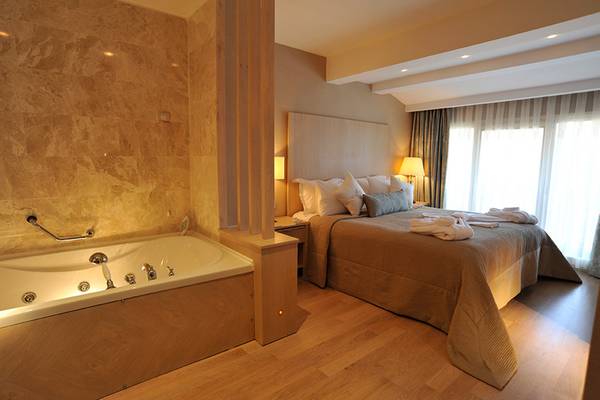 Schlafzimmer mit Badewanne im Marti Resort, inklusive Bett, Kissen, Decken und Badezimmerzubehör.