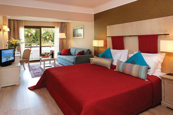 Hotelzimmer im Marti Resort mit rotem Bett, grauem Sofa, Fernseher und Balkonzugang.