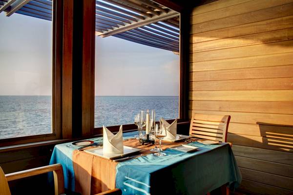 Tisch im Hotel Gangehi Island Resort mit Meerblick, gedeckt mit Geschirr, Gläsern und Kerzen.