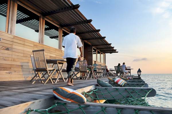 Terrasse des Gangehi Island Resorts bei Sonnenuntergang mit Gästen, die draußen sitzen.