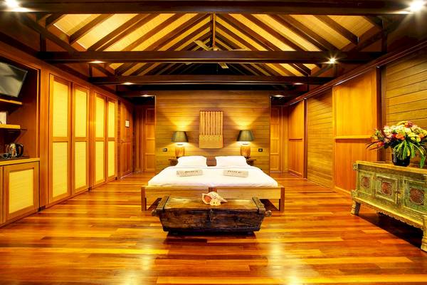 Schlafzimmer im Gangehi Island Resort mit Holzboden, Bett, Nachttischen, Lampen und Dekor.
