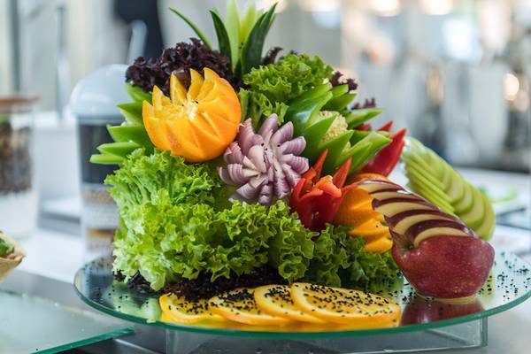 Obst- und Gemüsearrangement auf einem Teller, bestehend aus Apfel, Orange, Salat und anderen Gemüsesorten.