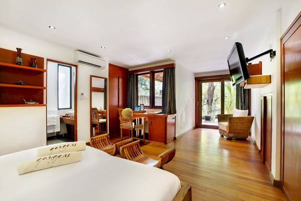 Innenansicht eines Zimmers im Gangehi Island Resort mit Bett, Holzmöbeln, Fernseher und Schreibtisch.