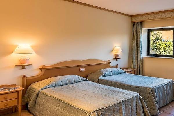 Doppelzimmer im Grand Hotel Gozo mit zwei Betten, Fenstern, Vorhängen, Lampen und einem Tisch mit Obst.