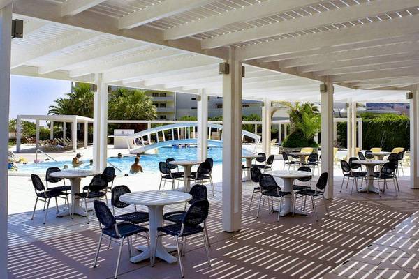 Poolbereich des Lindos White Hotel & Suites mit Tischen und Stühlen unter einem Pergoladach.