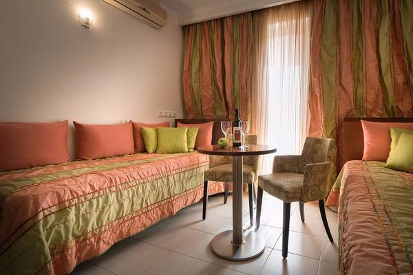Innenansicht eines Zimmers im Galaxy Beach Resort mit zwei Betten, einem Tisch und einem Fenster mit Vorhängen.