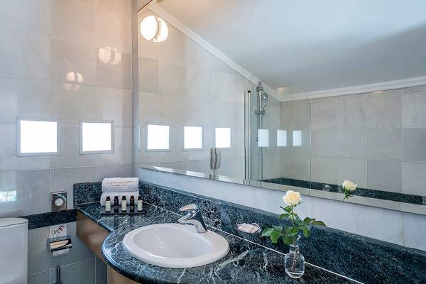 Badezimmer im Mitsis Lindos Memories Resort & Spa mit weißem Waschbecken, Marmorboden und großen Spiegel.