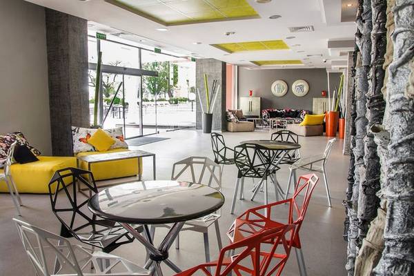 Lobbybereich des Gladiola Star Hotels mit bunten Stühlen und Tischen, gelben Sofas und einer Steinmauer.
