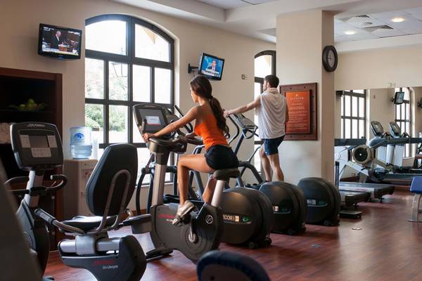 Eine Frau und ein Mann trainieren im Fitnessraum des Elysium Hotels auf einem Ellipsentrainer.