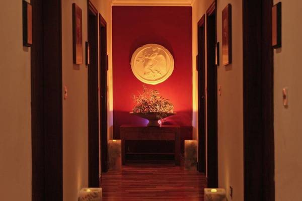 Innenansicht des Elysium Hotels, Flur mit roter Wand, zentrale Blumenvase und gedämpfte Beleuchtung.